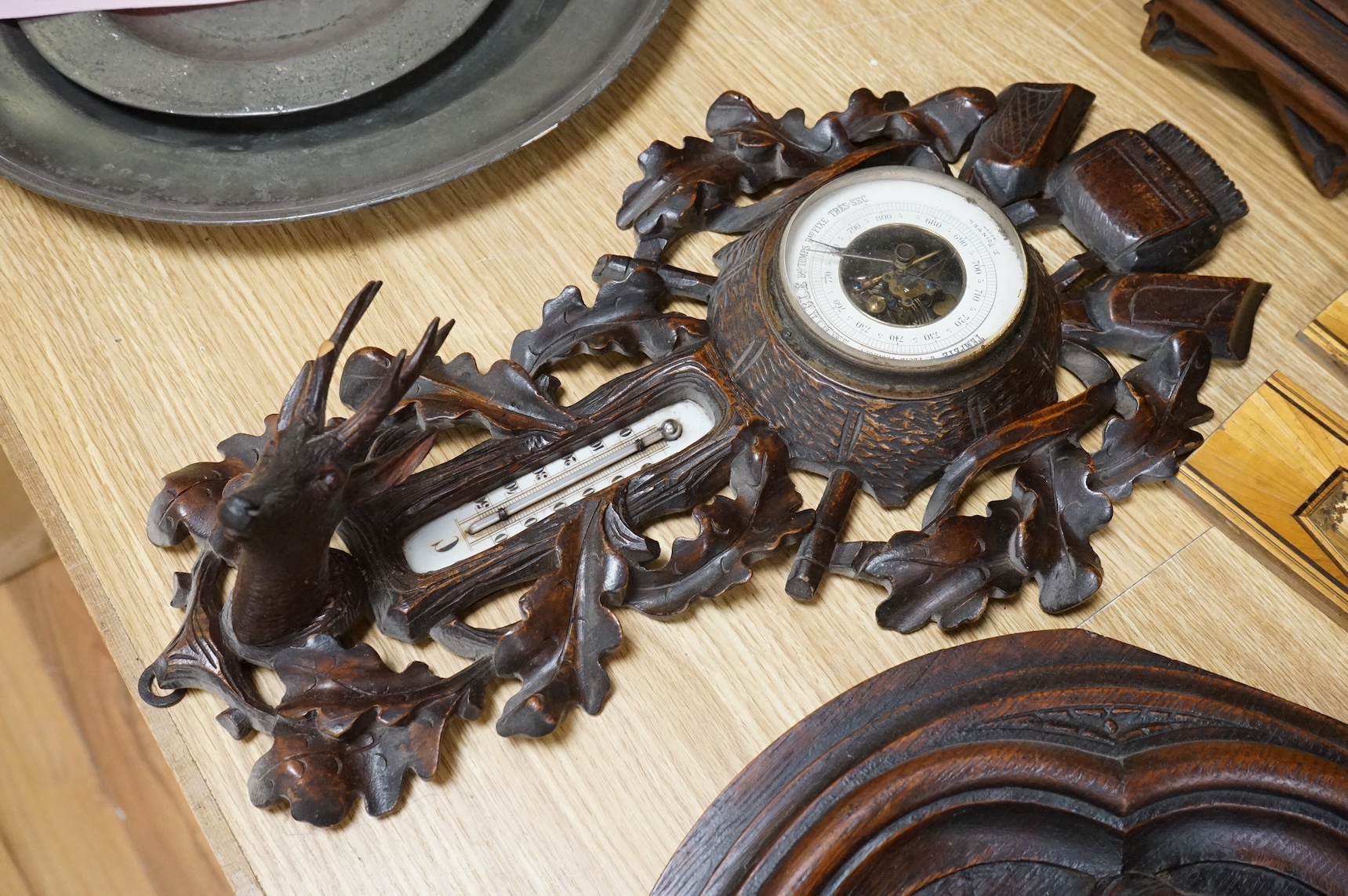A pair of Gothic revival oak wall plaques, a Black Forest carved barometer, a Virgin and child figure, an IHS embroidered panel, two straw worked panels and a carved finial, barometer 47cm high